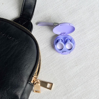 Purple earbuds in a case on a white surface with a black purse.